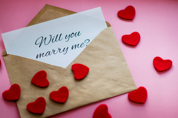 The envelope with a note "Will you marry me?" and carved hearts on pink background. Marriage proposal concept. - Photo, image