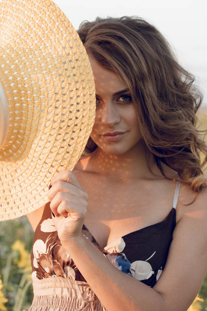 Young beautiful woman wearing a hat in a field of sunflowers - Foto, Imagen