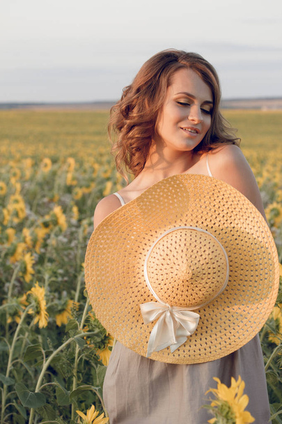 Young beautiful woman wearing a hat in a field of sunflowers - Fotoğraf, Görsel
