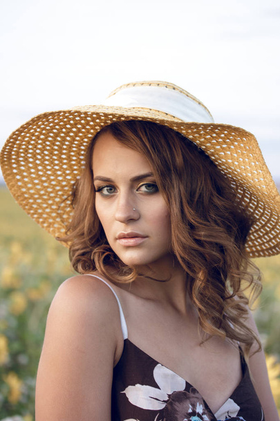 Young beautiful woman wearing a hat in a field of sunflowers - Фото, изображение