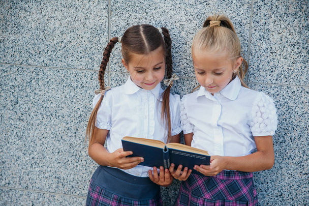 Pupils of primary school. Girls with backpacks and books near building outdoors. Beginning of lessons. First day of fall. - Photo, image