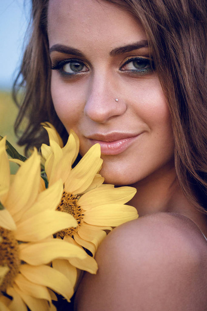 Young beautiful woman wearing a hat in a field of sunflowers - 写真・画像