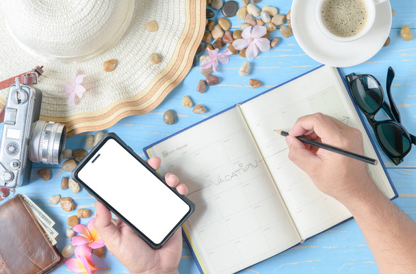 Homem escrevendo no livro planejador e segure o telefone celular na mesa de madeira azul, tomar vacaton e planejar viajar conceito
 - Foto, Imagem