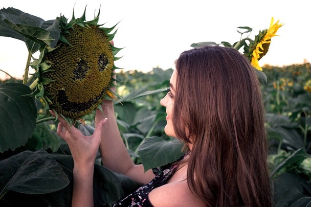 Menina de verão. Mulher jovem alegre bonita com girassol apreciando a natureza e rindo no campo de flores de sol de verão. Flare solar, raios de sol, sol brilhante. Luz de fundo
 - Foto, Imagem