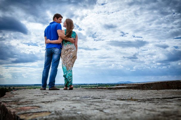 Šťastný mladý pár objímání stojící proti modré obloze, po celé délce - Fotografie, Obrázek