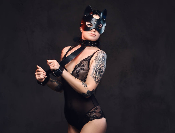sexy Frau trägt schwarze Dessous in bdsm Katzenledermaske und Accessoires posiert auf dunklem Hintergrund.  - Foto, Bild