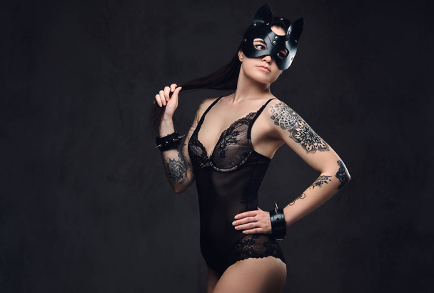 Femme sexy portant de la lingerie noire en cuir de chat BDSM masque et accessoires posant sur fond sombre
.  - Photo, image