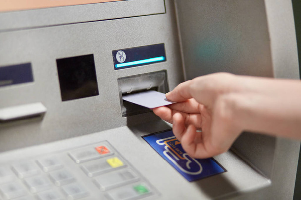Someone takes off money from outdoor bank terminal, inserts plastic credit card in atm machine, going to withdraw money and get salary. Cash machine. Modern technologies and innovations concept - Φωτογραφία, εικόνα