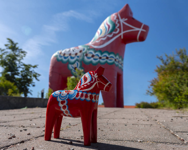 Крупним планом Червоної пофарбованої дерев'яної статуї Dala коня і найбільшим у світі кінь Dala в Avesta у фоновому режимі (літо 2018) - Фото, зображення