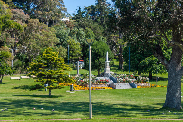 Burnie, Tasmania, Australie - 15 December 2009: Witte war memorial obelisk instellen in groen park met gele en rode bloemen centrum. - Foto, afbeelding