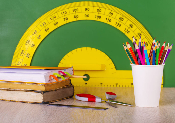 School concept: colore pencil, book, ruler, scissors and green chalkboard with yellow protractor - Photo, Image