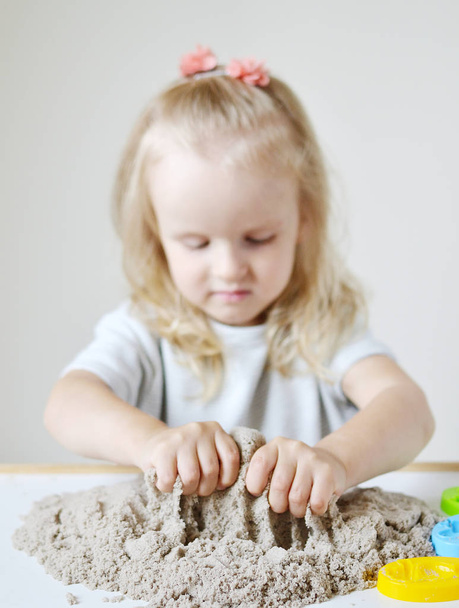 Pequena menina caucasiana brincando com areia cinética em casa Preparando-se para o desenvolvimento escolar Jogo de crianças
 - Foto, Imagem