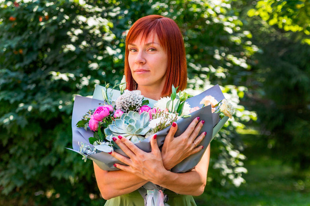 Portrait d'une belle jeune fille aux cheveux roux qui tient un bouquet spectaculaire et élégant de différentes fleurs. Cadeau d'un homme pour son anniversaire. Le concept du 8 mars, Journée internationale de la femme
 - Photo, image