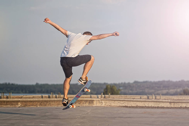 Skateboarder doing an ollie trick on background of blue sky. Active lifestyle. - 写真・画像