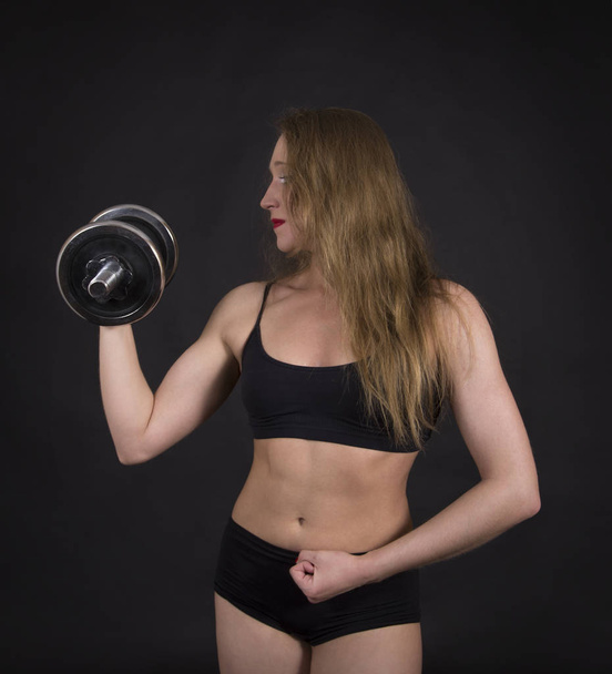 A young woman engaged in fitness with dumbbells. Studio shot on black background. Isolated image. - Photo, Image