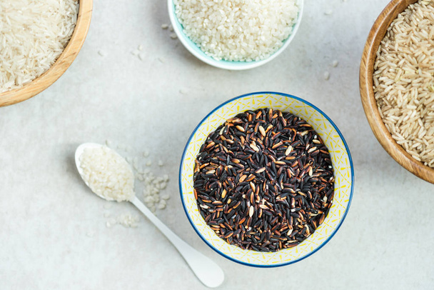 Different types of rice in wooden bowls such as basmati, brown and black on grey background - Foto, immagini