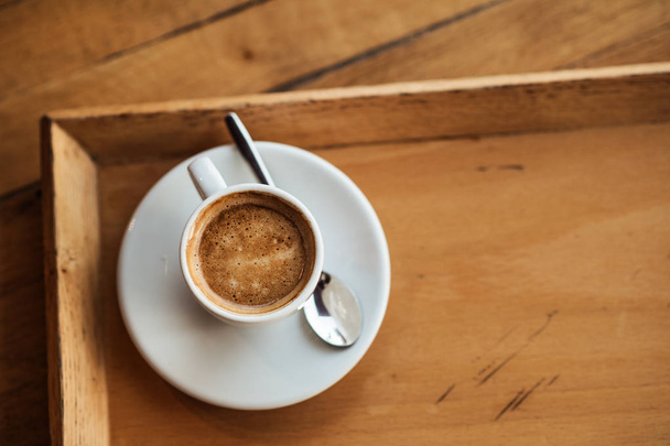 top view of white Cup with black coffee on a white saucer and teaspoon on wooden background with copyspace on the right - Fotó, kép