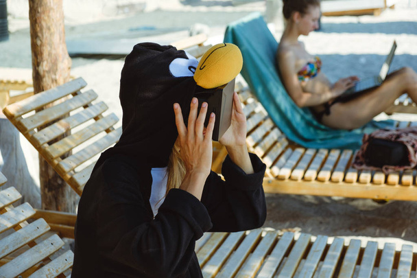 Crazy young beautiful skinny woman in penguin costume with VR glasses on the summer beach - Photo, Image