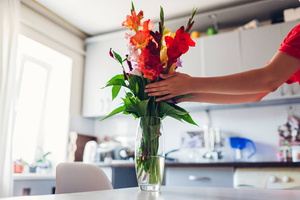 Vrouw zet rode bloemen in vaas. Jonge huisvrouw verzorgen van gezelligheid in de keuken. Moderne keukenontwerp. Wit en zilver keuken - Foto, afbeelding