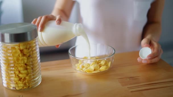 Woman hands pouring milk into glass bowl of corn flakes. Preparing breakfast - Filmati, video