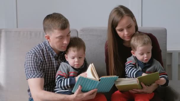 Family mom, dad and two twin brothers read books sitting on the sofa. Family reading time. - Metraje, vídeo