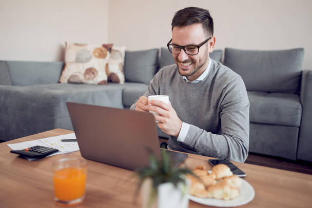 Portret van een man thuis werken op een laptop en drinken koffie. - Foto, afbeelding