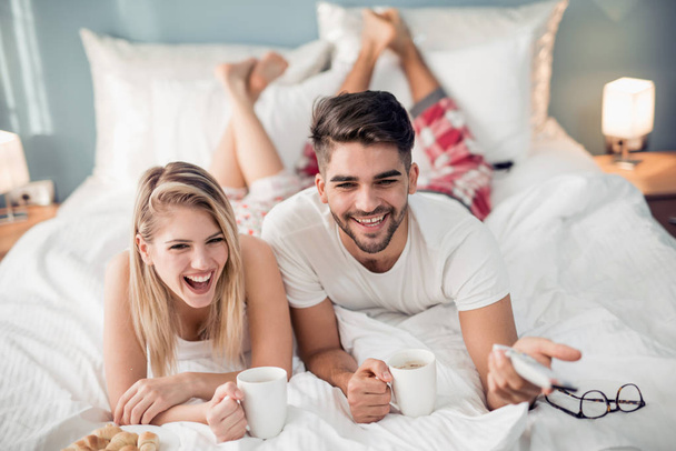 Jeune couple se réveillant et regardant la télévision sur le lit à la maison
. - Photo, image