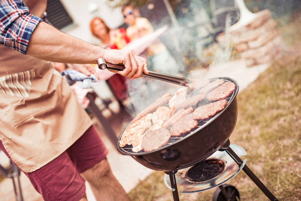 Hombre cocinar carne en la parrilla de barbacoa para su familia en la fiesta al aire libre de verano, de cerca
. - Foto, imagen