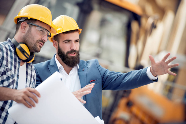 Two engineer builders with plan at construction site. - Φωτογραφία, εικόνα