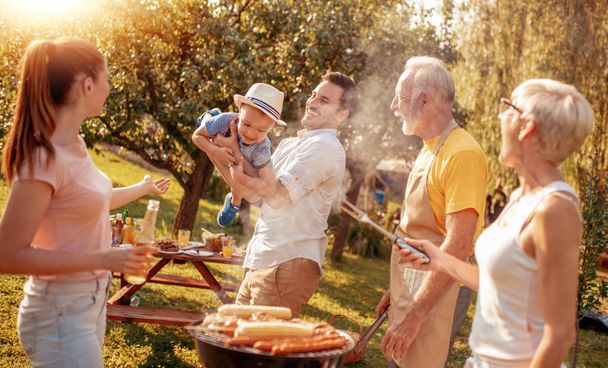 Glückliche große Familie versammelte sich um den Grill beim Picknick. Freizeit, Essen, Familien- und Urlaubskonzept. - Foto, Bild
