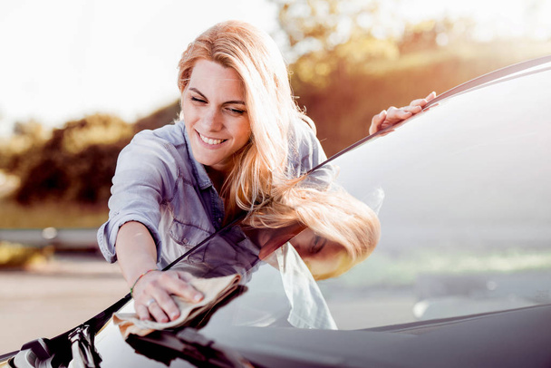 Νεαρή γυναίκα καθαρισμού το αυτοκίνητό της σε εξωτερικούς χώρους. - Φωτογραφία, εικόνα