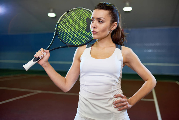 Taillenhoch Porträt einer schönen jungen Frau, die mit Tennisschläger posiert und selbstbewusst in den Innenhof blickt - Foto, Bild