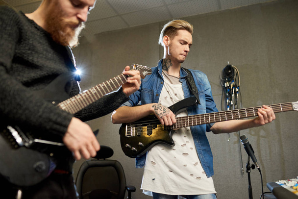 Jeunes musiciens élégants jouant des guitares et créant de nouvelles chansons dans un studio d'enregistrement de musique moderne
.  - Photo, image