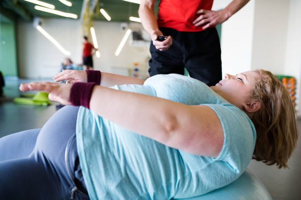 Seitenansicht Porträt einer übergewichtigen jungen Frau, die sich beim Crunchen auf dem Fitnessball im Fitnessstudio mit Anstrengung anstrengt - Foto, Bild