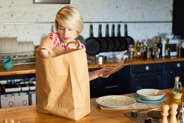 Mladá žena s papírové tašky a seznam produktů na kuchyni - Fotografie, Obrázek