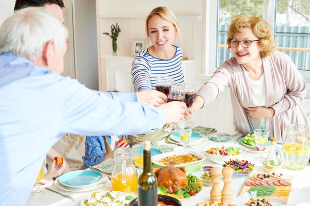 Portrait of happy two generation family enjoying dinner clinking glasses at festive table with delicious dishes and laughing during holiday celebration in modern sunlit apartment, copy space - Foto, Bild