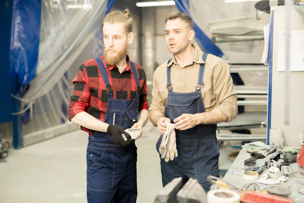 Nuoret ammattimaiset miespuoliset autoteknikot tarkastelevat jotain tarkkaavaisesti valmistautuessaan töihin korjaamossa.
 - Valokuva, kuva