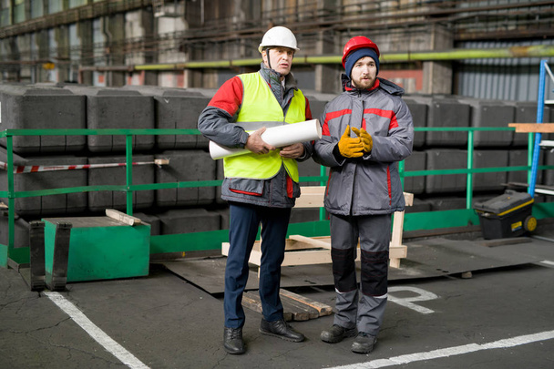 Ολόσωμο πορτρέτο του δύο μηχανικούς που φοράει hardhats συζητώντας κατασκευής σε σύγχρονο βιομηχανικό εργαστήριο, αντίγραφο χώρου - Φωτογραφία, εικόνα