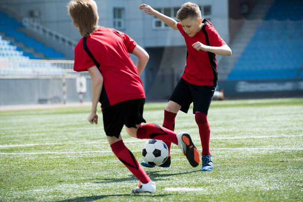 Täyspitkä muotokuva kaksi teini pojat pelaavat jalkapalloa stadionilla aikana junior joukkue käytännössä, kopioi tilaa
 - Valokuva, kuva