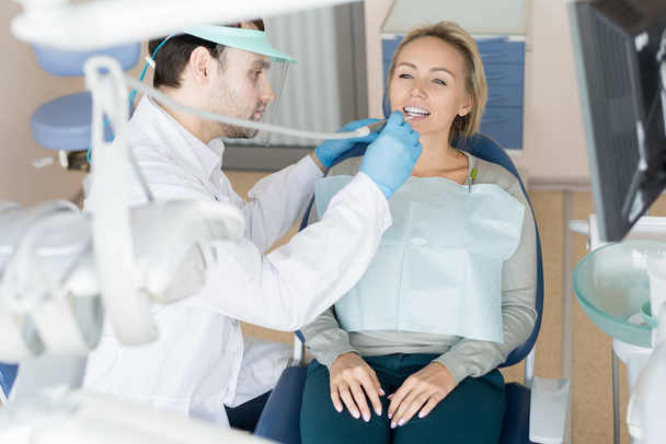 Professionele tandarts in uniform boren tand van mooie vrouw zitten in de stoel met bezoek - Foto, afbeelding