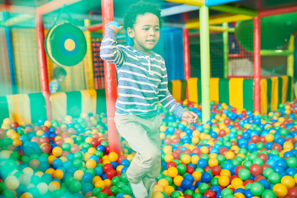 Ritratto di carino ragazzo afroamericano che gioca nella fossa delle palle, si diverte in un grande centro di gioco al coperto, colpito attraverso la rete
 - Foto, immagini