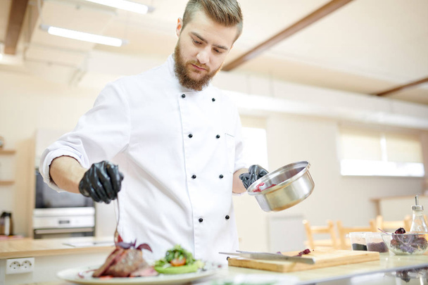 Retrato del guapo chef profesional que sirve plato de carne mientras cocina en la cocina moderna del restaurante
 - Foto, imagen