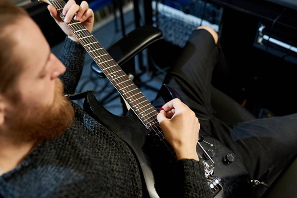 De arriba plano de barbudo hombre sentado en silla con la guitarra y la creación de una nueva canción en estudio de sonido
.  - Foto, imagen