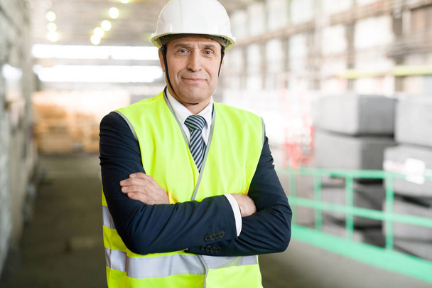 Waist up portrait of mature engineer wearing hardhat and business suit posing looking at camera and standing with arms crossed in workshop of modern industrial plant, copy space - Фото, зображення
