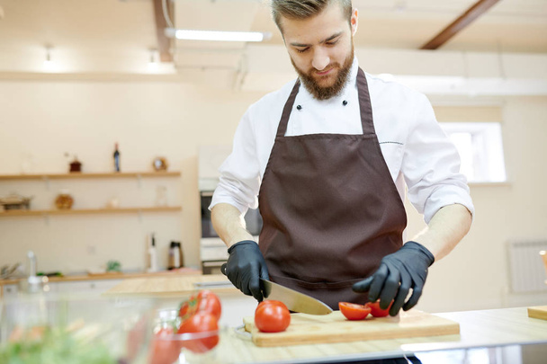 Waist up portrait of handsome bearded chef cooking salad in restaurant kitchen cutting vegetables with big knife, copy space - Photo, Image