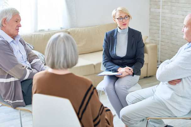 Portret van blonde vrouwelijke psychiater bril groepstherapie sessie leidt voor senior mensen zitten in cirkel in bejaardentehuis, kopie ruimte - Foto, afbeelding