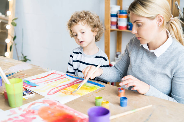 Little boy looking at how teacher helping him to paint a picture in art lesson - Foto, Imagen
