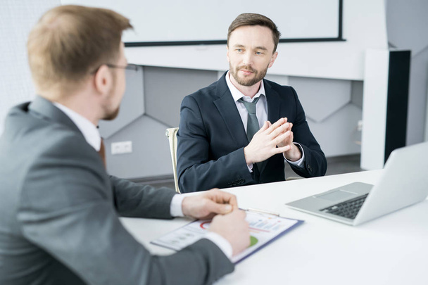 Portret van knappe zakenman luisteren naar partner tijdens de bijeenkomst in moderne kantoren - Foto, afbeelding