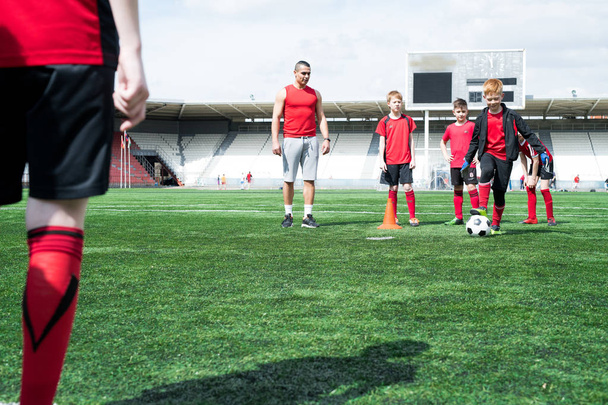 Full length portrait of junior football team practice, focus on red haired teenage boy leading ball, copy space - Фото, зображення