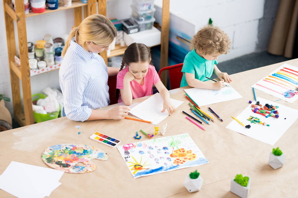 Két gyermek élvezi a művészeti és kézműves lecke fiatal tanárral az iskolában fejlesztés magas szög portréja - Fotó, kép